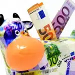 Mains anonymes comptant des billets euro près d'une petite tirelire sur une table