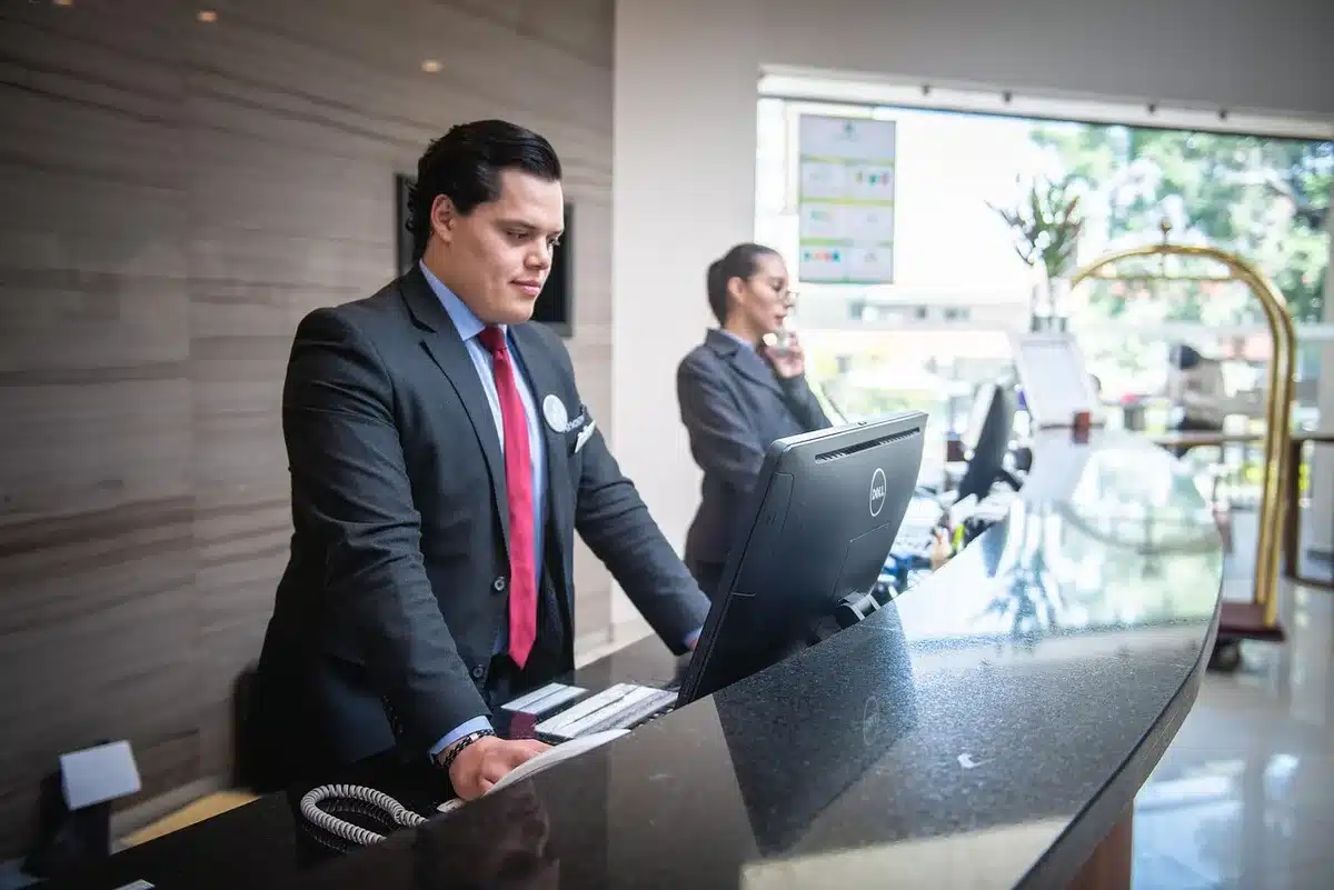 Des clients avec bagages à la réception d'un hôtel moderne, personnels en arrière-plan.